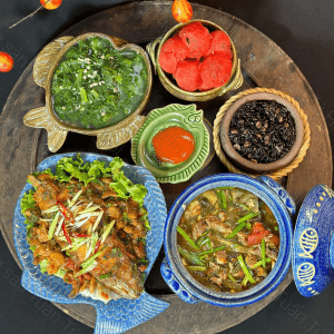 Mâm gỗ tròn bày cá chiên, niêu kho, rau xào và cà chua
